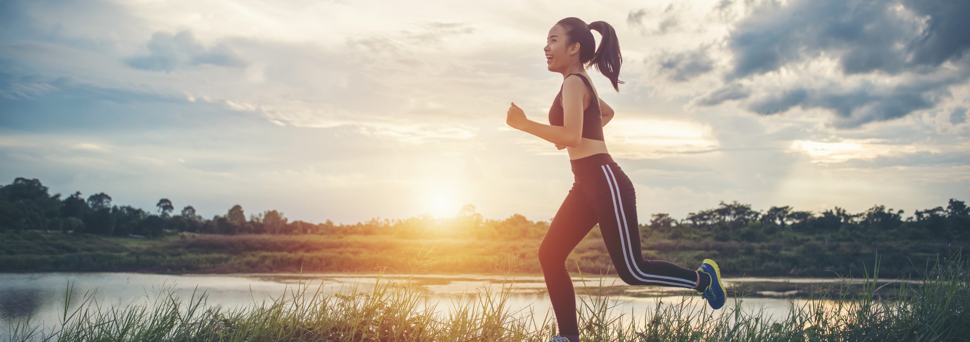 Smiling young woman jogging beside a lake at sunset